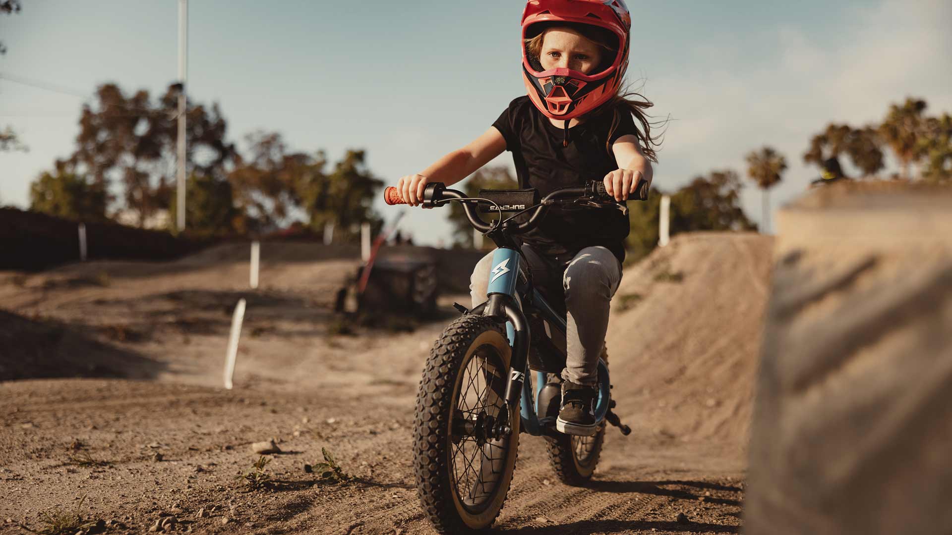 Young girl riding on a blue SUPER73-K1D in a helmet on a dirt track